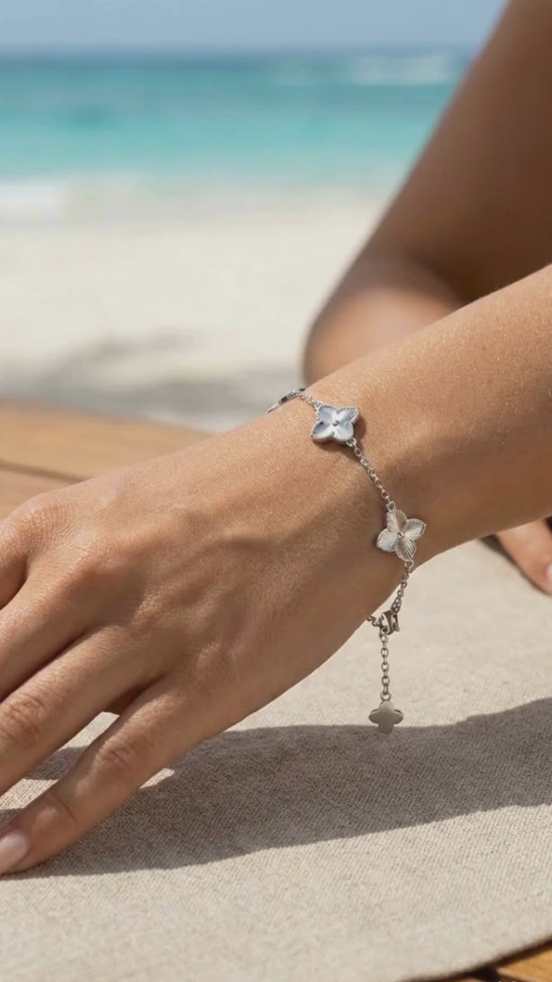 Jewelry stacking inspiration: a gold textured clover bracelet layered with a luxury watch and thin gold bangles.