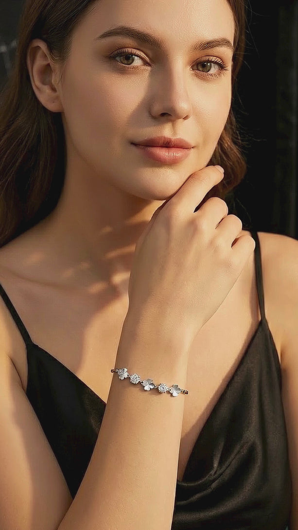 Video of a model in a black evening gown elegantly moving her wrist, demonstrating the maximum light reflection of the Hearts and Arrows cut CZ stones on the silver clover bracelet.