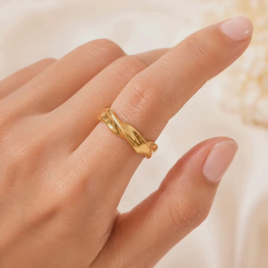 Close-up of gold wavy ring on finger showing polished curved water wave design