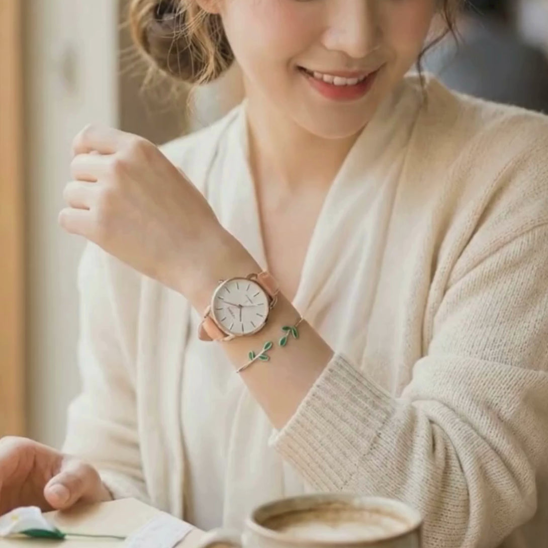 Lifestyle video capturing the romantic blush pink botanical watch and mint leaf bangle set in motion, styled with a casual outfit in a relaxing wooden cafe environment.