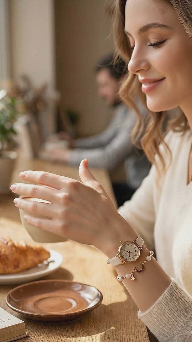 Lifestyle video of a model in a relaxing wooden cafe, showcasing the fluid movement and delicate sparkle of the minimalist off-white celestial watch and the gold-tone crystal moon and star bracelet.