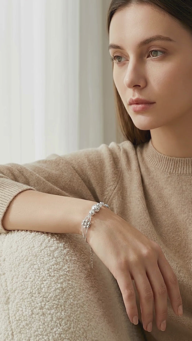 Lifestyle video showing a model in a cozy soft home environment wearing casual clothes, demonstrating the fluid movement and brilliant shine of the S999 fine silver triple layered bracelet.