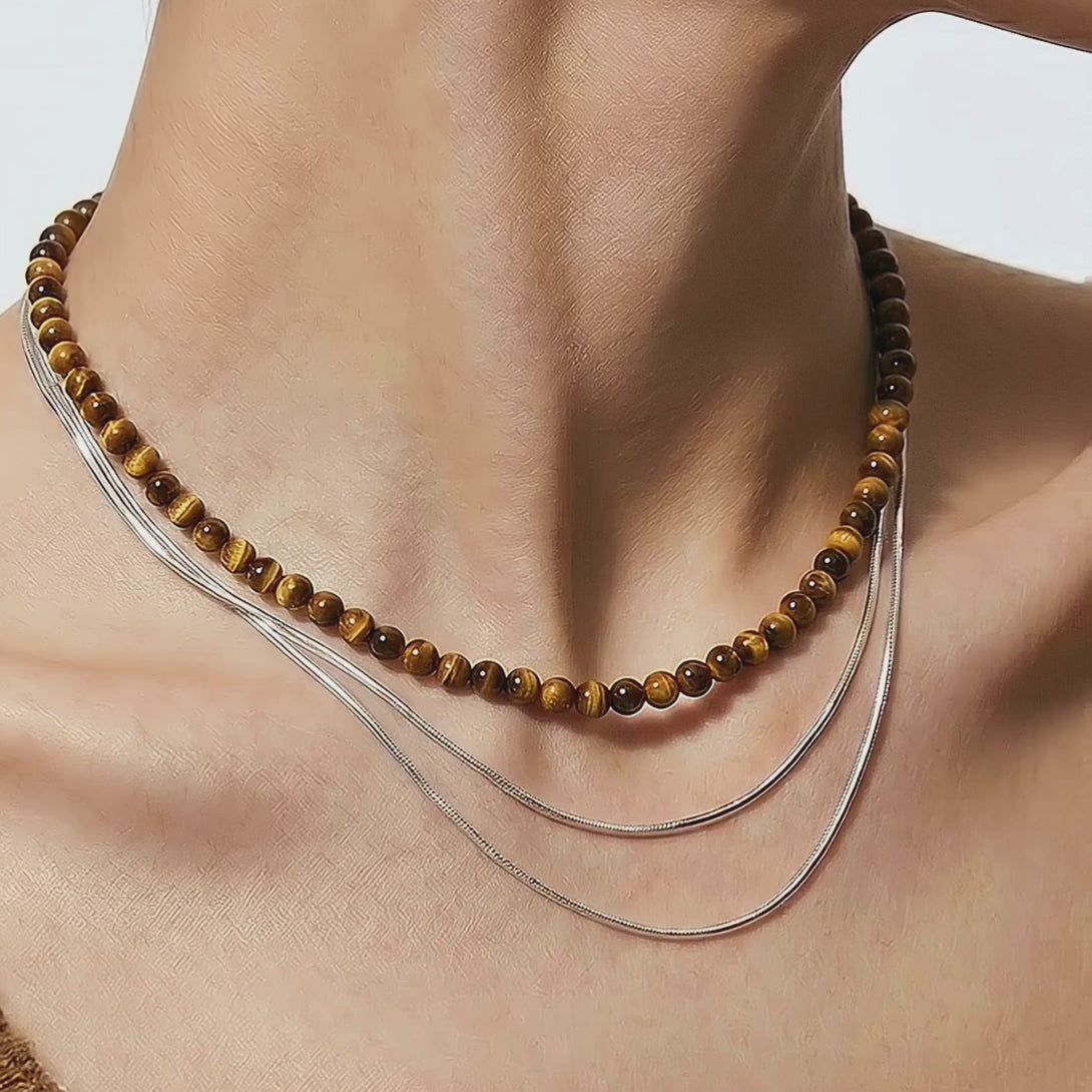 Cinematic video demonstrating how to style the dainty 4mm natural tiger eye beaded necklace with silver chains and a cozy brown knit sweater.